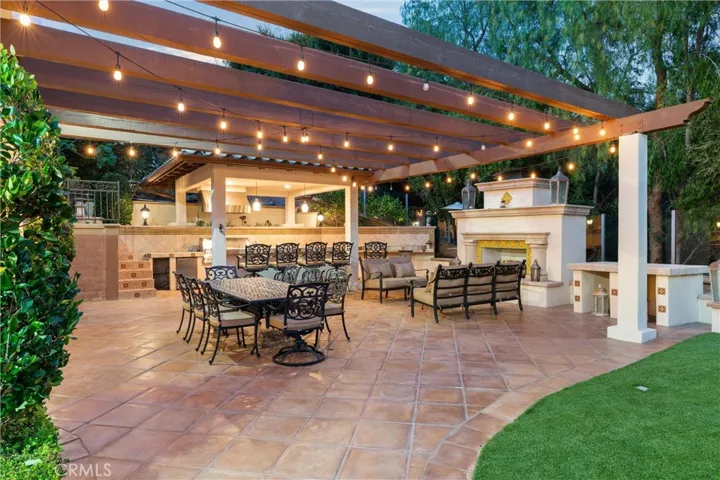 Expansive outdoor entertaining space featuring a fireplace, built-in BBQ, bar seating, and multiple gathering areas.
