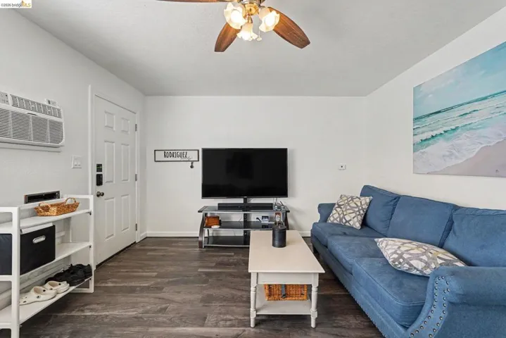 Living area featuring wood-finish flooring, a white paneled door with smart lock, and a ceiling fan with integrated lighting