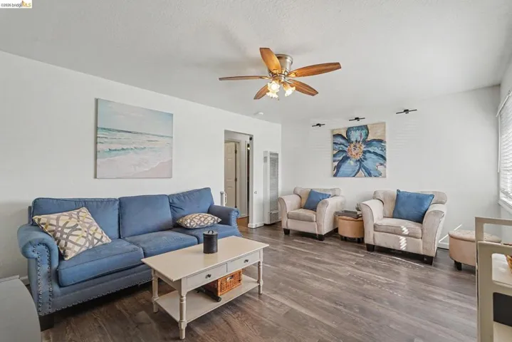 Living area featuring wood-finish flooring, a ceiling fan with integrated lighting, and white walls