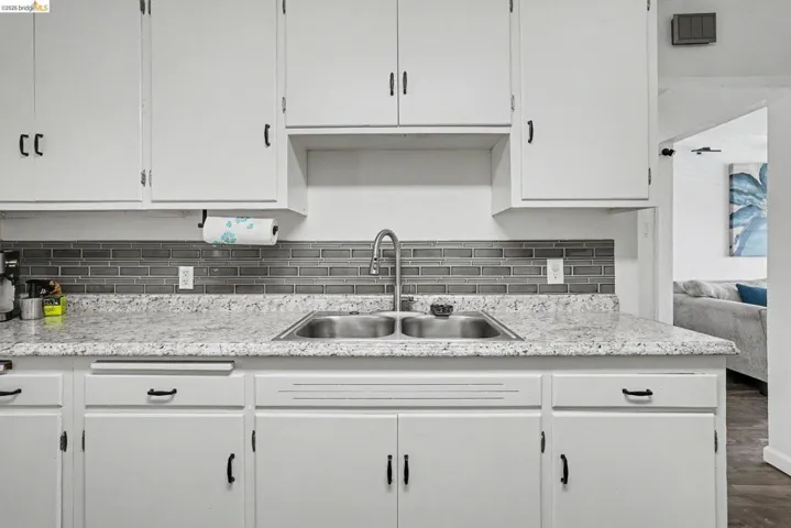 Kitchen featuring white cabinetry, a dual basin stainless steel sink, a modern pull-down faucet, a grey subway tile backsplash, and speckled countertops