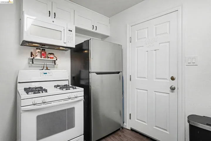 Kitchen featuring white cabinetry, an over-the-range microwave, a gas range, and a stainless steel refrigerator
