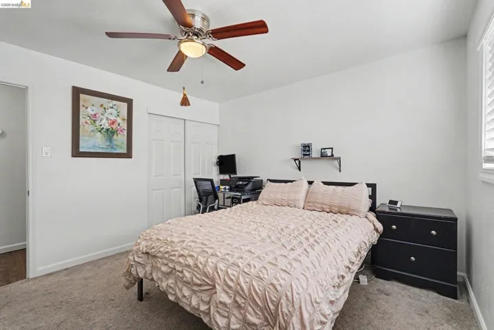 Carpeted bedroom featuring a ceiling fan with integrated lighting, a window with blinds, and white bi-fold closet doors
