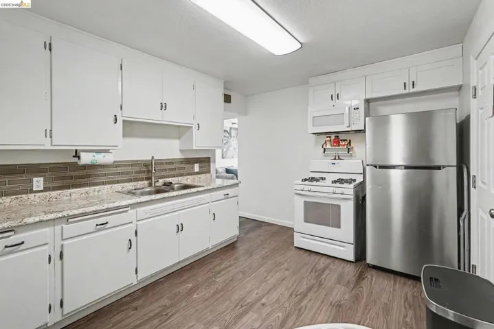 Kitchen featuring white cabinetry, a stainless steel refrigerator, white range, built-in microwave, and wood-finish flooring