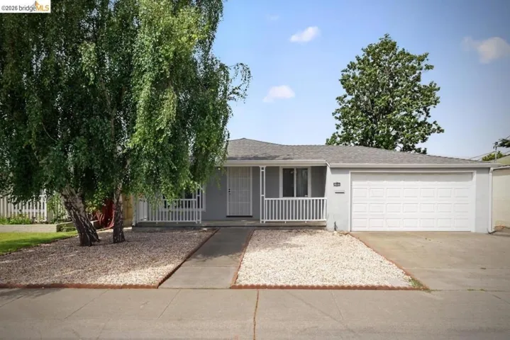 Single-story residence featuring a two-car garage, front porch with white railing, and a light gray exterior