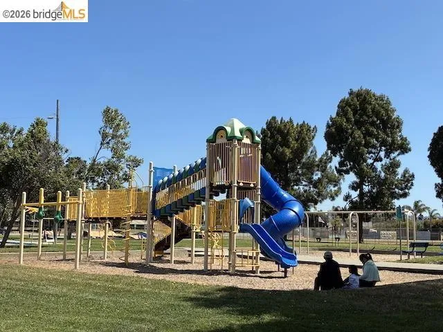 Expansive park setting featuring a large blue and yellow playground structure with multiple slides and climbing elements