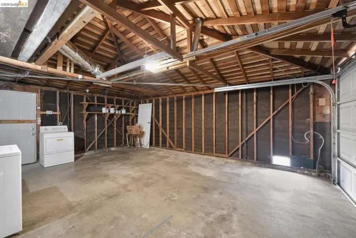 Attached garage with exposed wood beam ceiling, concrete flooring, overhead lighting, and built-in shelving