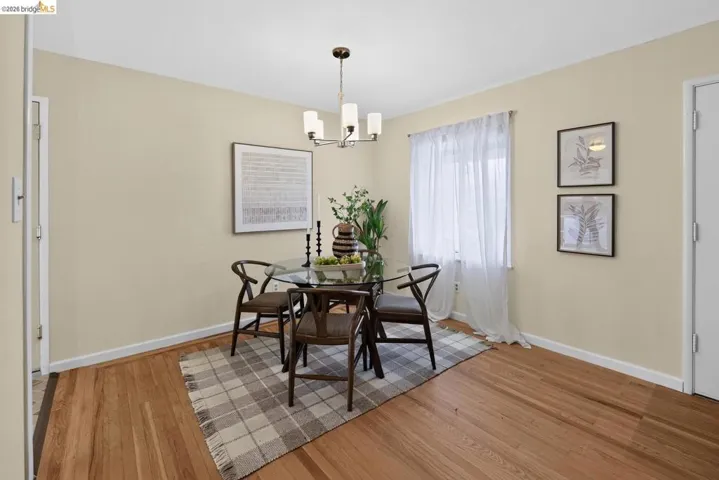 Dining space featuring wood-finish flooring, light-toned walls, and a window with sheer drapes