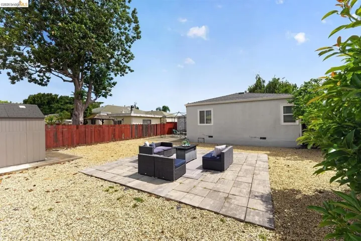 Paved patio area, spacious gravel landscaping, privacy fencing, mature trees, and an outdoor storage shed