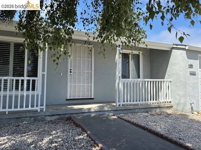 Light gray stucco exterior featuring white window frames and a white metal security door