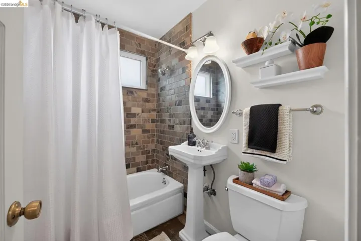 Bathroom featuring a pedestal sink, oval mirror, and a tub-shower combination with a textured tile surround