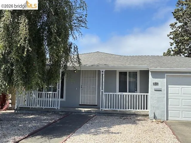 Single-story residence featuring a covered front porch with white railing, a light gray stucco exterior, and a gravel front yard with a concrete pathway