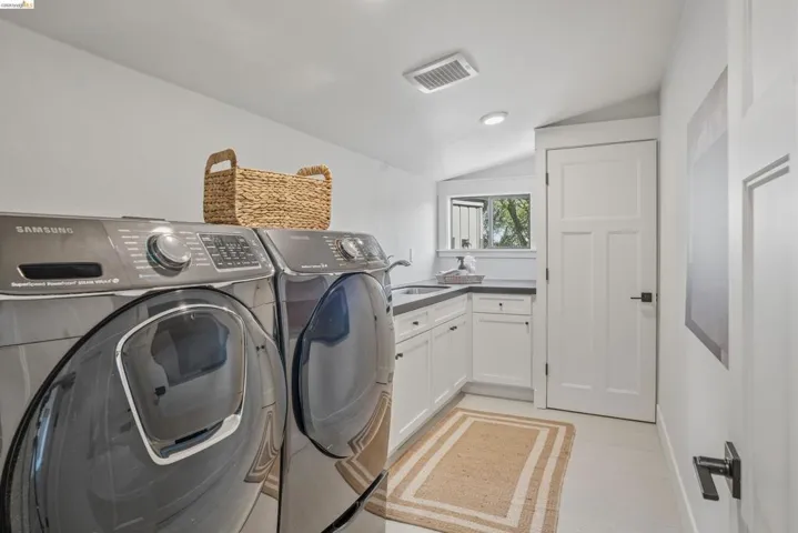 Dedicated laundry area featuring white cabinetry, dark countertops, an integrated sink, and white flat-panel doors with matte black hardware