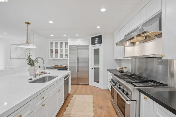 Modern kitchen featuring a large central island with an undermount sink, stainless steel appliances, white cabinetry, and wood-finish flooring