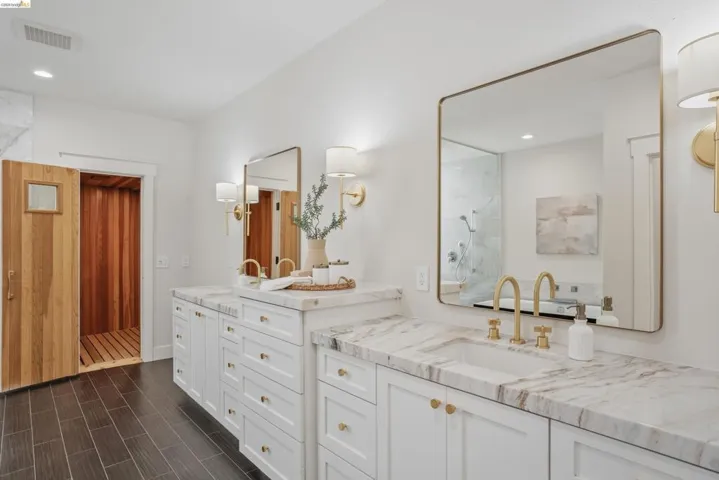 Dual vanity with white cabinetry, gold-toned hardware, and stone countertops