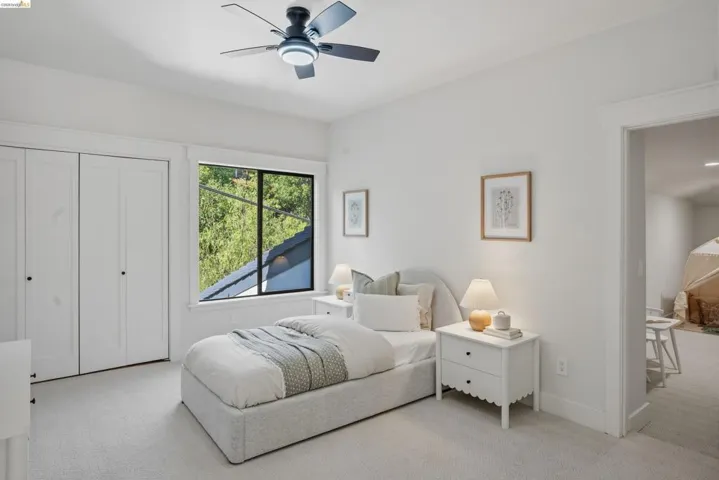 Bright bedroom featuring a large window, integrated ceiling fan with lighting, ample closet space, and plush carpeting