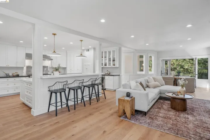 Expansive room featuring light wood-finish flooring, recessed lighting, and a kitchen with white cabinetry, a central island, and a breakfast bar with pendant lighting