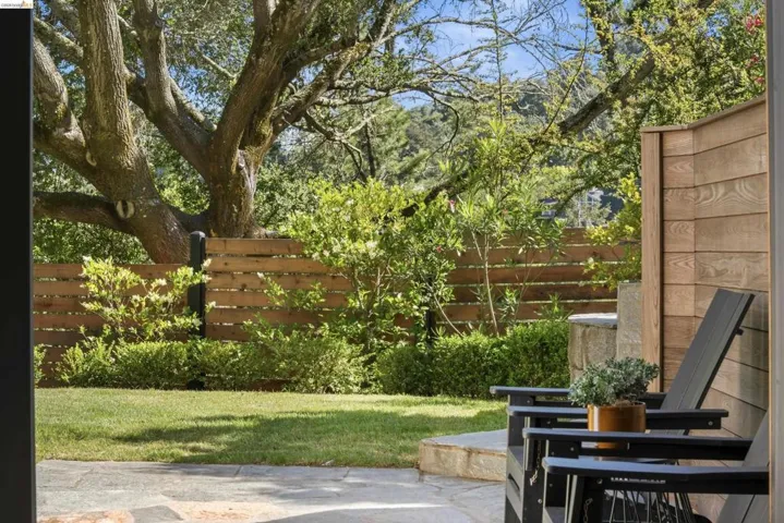 Stone patio area featuring a level lawn, mature tree, and horizontal wood fencing