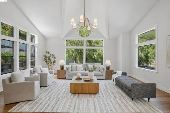 Living area featuring vaulted ceilings, wood-finish flooring, a contemporary chandelier, and extensive fenestration with transom windows