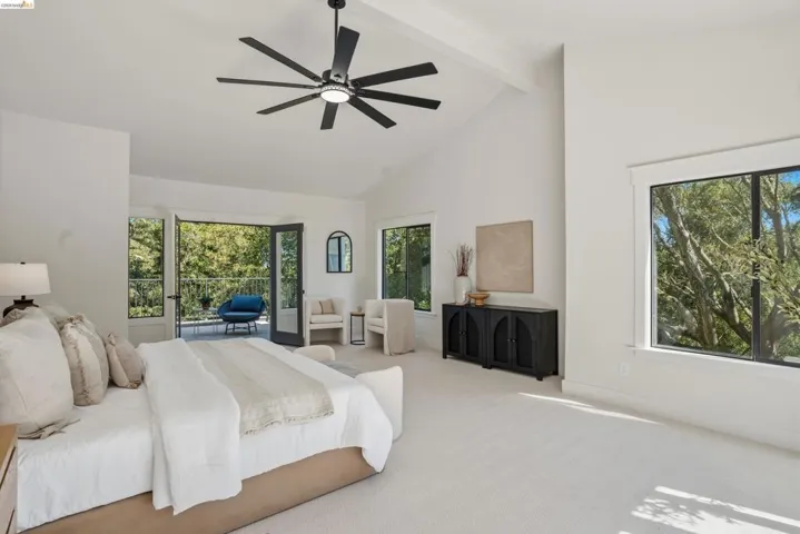 Spacious room featuring vaulted ceilings, a large ceiling fan with integrated lighting, a built-in balcony with a black railing, and multiple windows with black trim