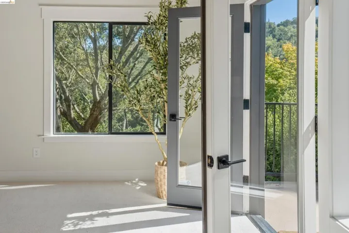 Light-filled room featuring plush carpet flooring, a large window with black trim, and a glass-paneled door opening to a balcony with black railings