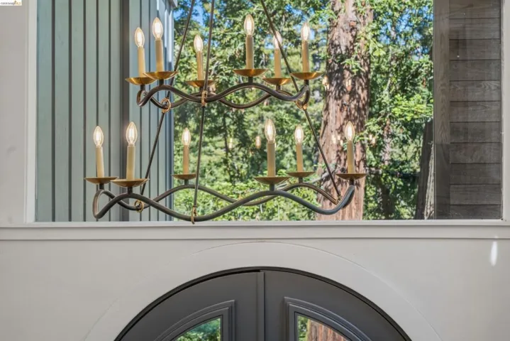 Wrought iron chandelier with brass accents, set against a backdrop of mature trees