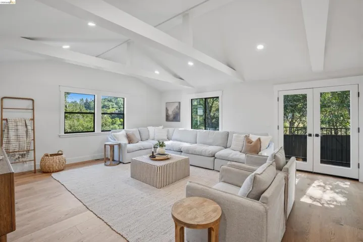 Spacious room featuring vaulted ceilings with exposed beams, recessed lighting, light wood-finish flooring, and white walls