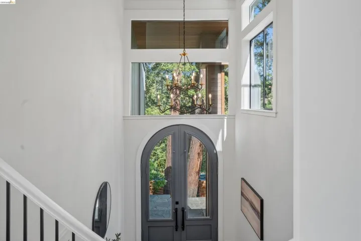 Double arched entry doors with transom windows, a multi-pane glass chandelier, and white-painted walls