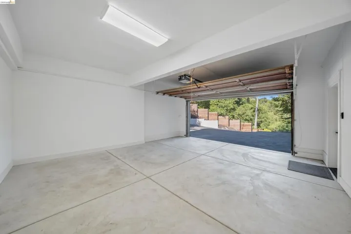 Spacious garage featuring a concrete floor, bright overhead lighting, painted white walls, and an automatic garage door opener