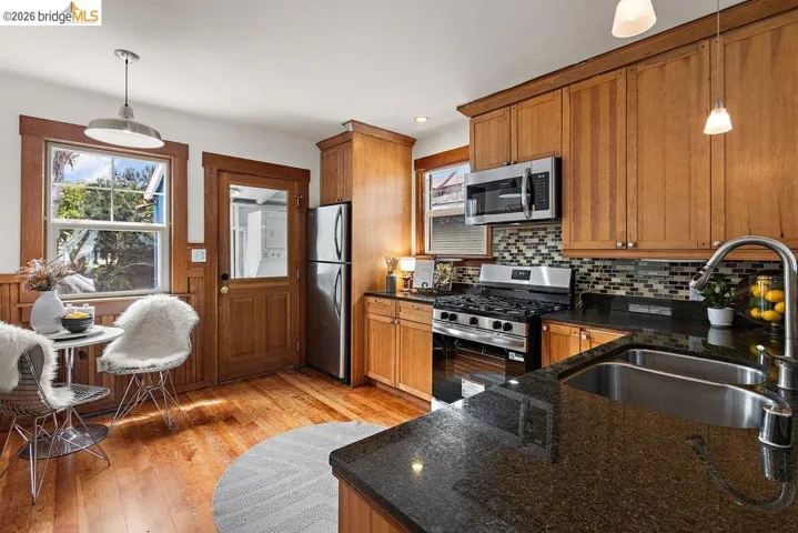 Kitchen featuring wood-finish flooring, dark countertops, a mosaic tile backsplash, wood cabinetry, and stainless steel appliances