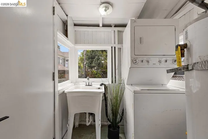 Dedicated laundry area featuring a stacked washer and dryer unit, utility sink with chrome faucet, and a window providing natural illumination