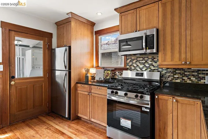 Kitchen featuring wood-finish cabinetry, stainless steel appliances, dark countertops, and a mosaic tile backsplash