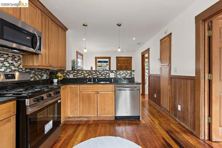 Kitchen with stainless steel appliances, wood-finish cabinetry, dark countertops, and mosaic tile backsplash