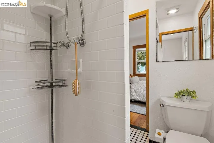 Shower with white subway tile surround, corner shelving unit, and wall-mounted shower fixtures