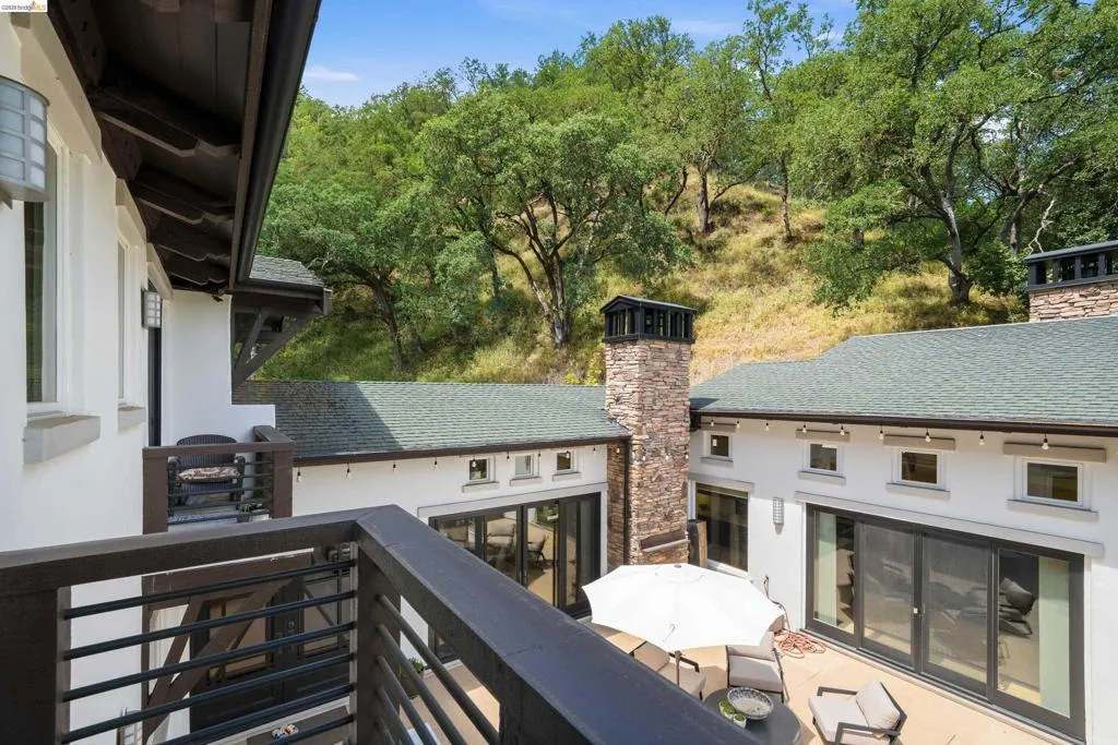 Exterior patio with multiple sliding glass doors, a stone-clad chimney, and a green shingle roof