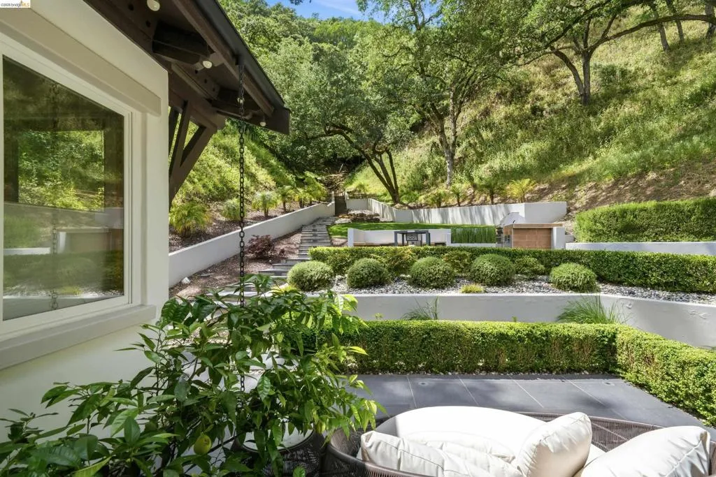 Tiered hillside landscaping featuring structured shrubbery, a paved patio area, and a built-in outdoor cooking station