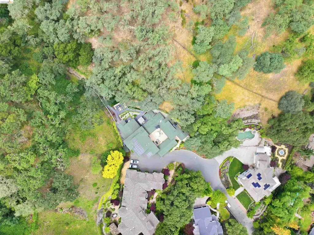 Aerial view showcasing a property with a multi-level green roof, an expansive paved driveway, and solar panels