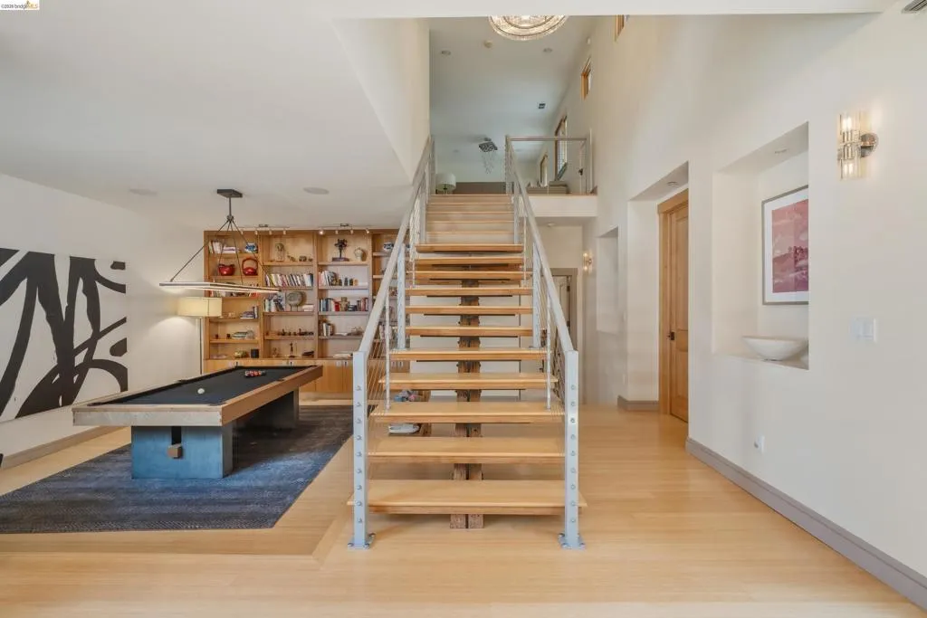 Open-tread staircase with metal railings, hardwood flooring, built-in shelving, high ceilings, and a second-story landing