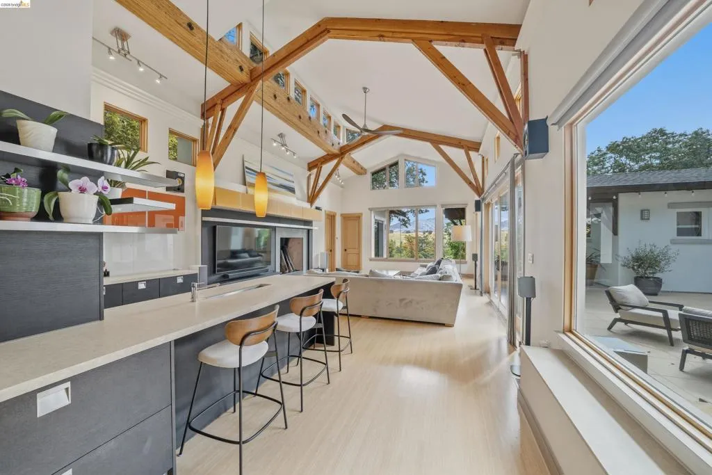 Open-concept kitchen and living area featuring exposed wood ceiling beams, light wood-finish flooring, and expansive glass sliding doors
