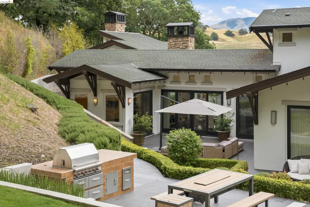 Expansive outdoor patio featuring an integrated outdoor kitchen with built-in grill, a dining area, and a lounge space
