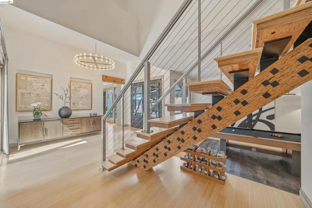 Open-tread staircase with cable railing, light wood-finish flooring, vaulted ceilings, and a contemporary chandelier