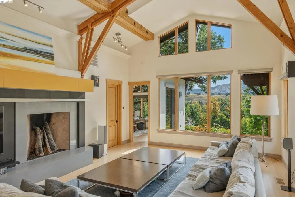 Spacious living area featuring exposed wood beam vaulted ceilings, light wood-finish flooring, and a contemporary fireplace with a large hearth