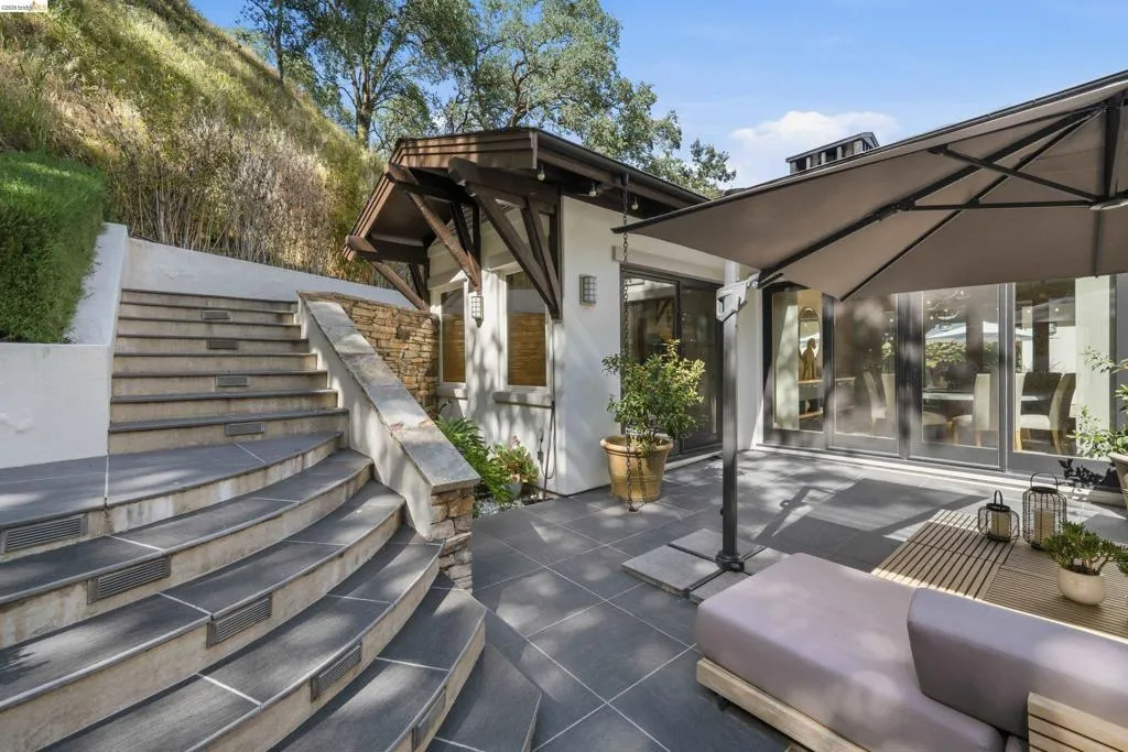 Expansive outdoor patio with dark tile flooring, stone-clad retaining wall, and curved staircase with integrated lighting