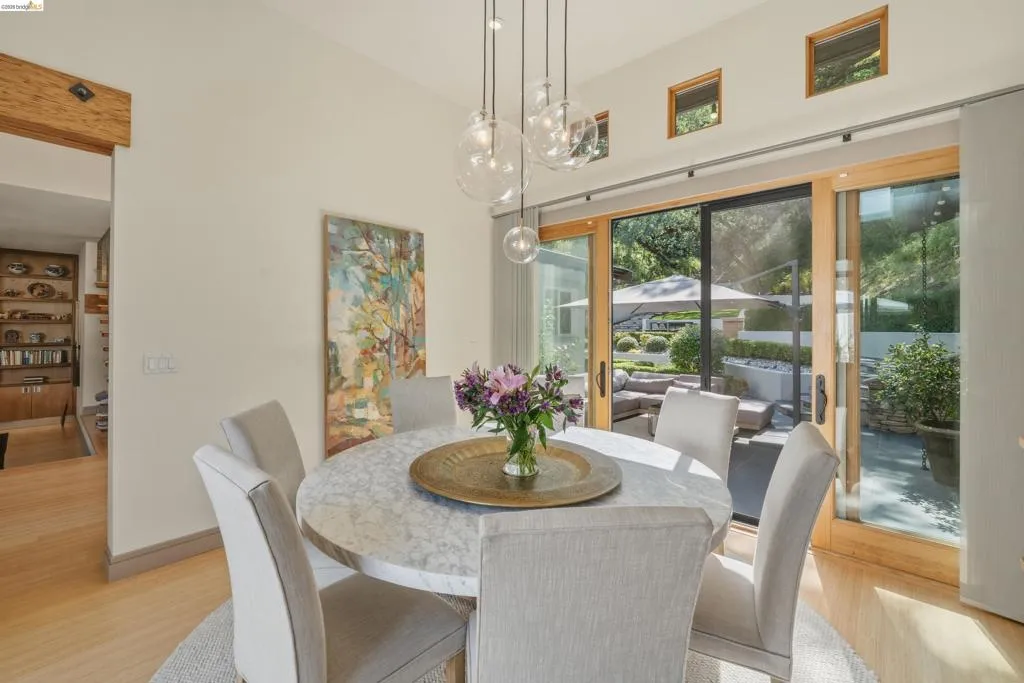 Dining area featuring a round stone-finish table, suspended glass pendant lighting, light wood-finish flooring, and large sliding glass doors opening to the exterior patio