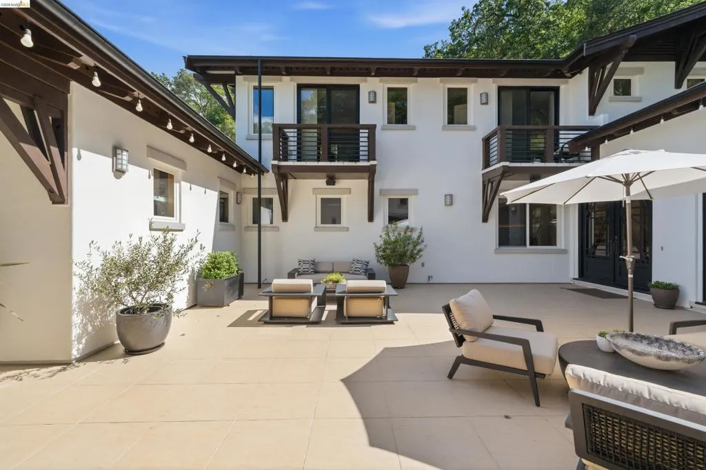 Spacious outdoor patio featuring light-toned large format tile, multiple access points to the residence, and private second-story balconies with dark wood railings