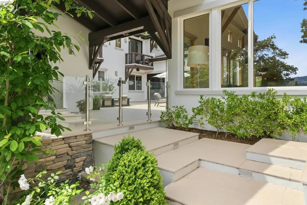 Exterior patio featuring stone steps, glass panel railing, and surrounding landscaping