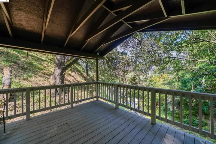 Covered wood-finish deck with railing and a natural treed backdrop