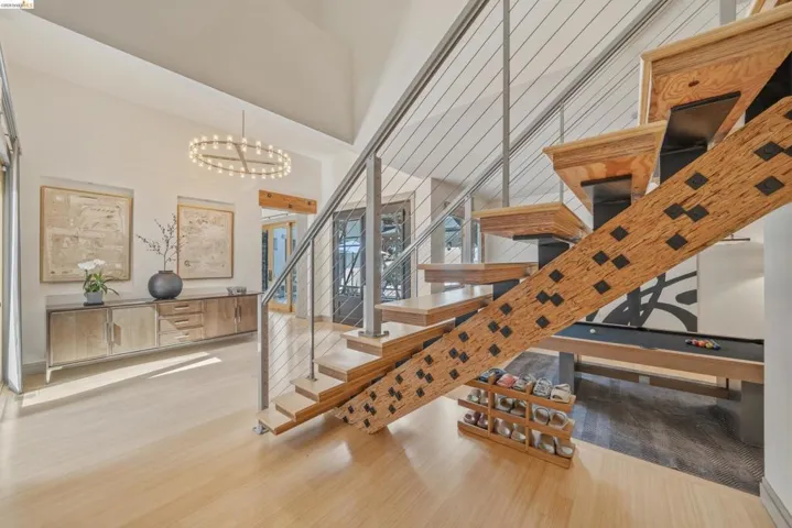 Open-tread staircase with cable railing, light wood-finish flooring, vaulted ceilings, and a contemporary chandelier