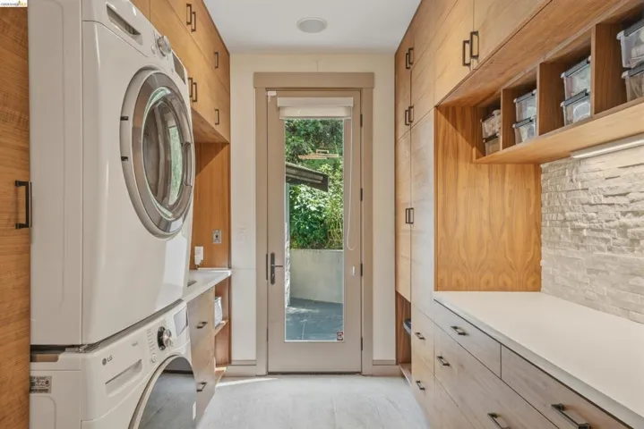 Dedicated laundry area featuring stacked appliances, extensive wood-finish cabinetry, white countertops, and a stone-clad backsplash