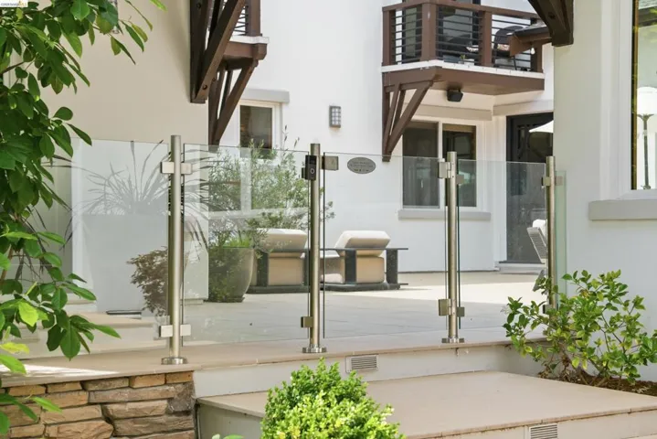 Outdoor patio space featuring a contemporary glass railing system with stainless steel posts, stone block retaining wall, and light-colored paving