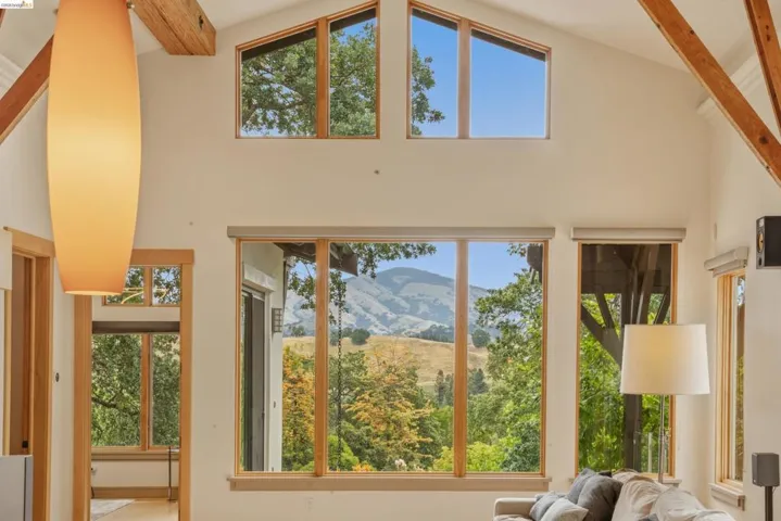 Vaulted ceiling featuring exposed wood beams, extensive natural wood-framed windows, and a prominent mountain and tree landscape visible through the windows